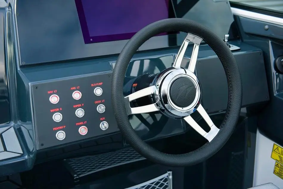 Boat dashboard featuring a chrome steering wheel, control buttons, and a digital display screen.